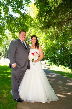 A wedding couple pose for portraits at a park outdoors on their wedding day. The bride and groom are both very happy after just tying the knot and getting hitched.