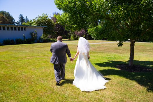 A bride and groom walk away from the camera holding hands at this outdoor wedding venue location in a park after just tying the knot.