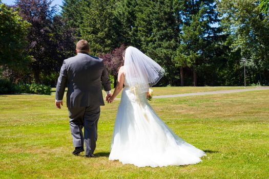 A bride and groom walk away from the camera holding hands at this outdoor wedding venue location in a park after just tying the knot.