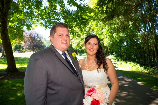 A wedding couple pose for portraits at a park outdoors on their wedding day. The bride and groom are both very happy after just tying the knot and getting hitched.