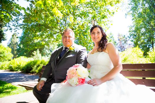 A wedding couple pose for portraits at a park outdoors on their wedding day. The bride and groom are both very happy after just tying the knot and getting hitched.