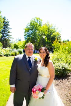 A wedding couple pose for portraits at a park outdoors on their wedding day. The bride and groom are both very happy after just tying the knot and getting hitched.