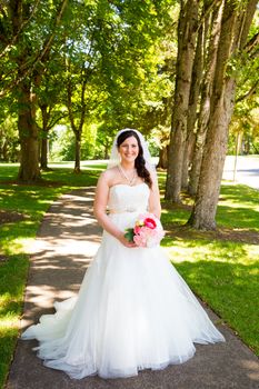 A bride poses for some portraits while wearing her wedding dress at a park outdoors just before here wedding ceremony.