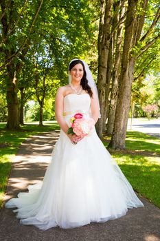 A bride poses for some portraits while wearing her wedding dress at a park outdoors just before here wedding ceremony.