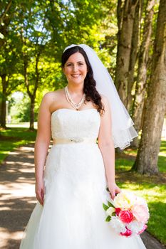 A bride poses for some portraits while wearing her wedding dress at a park outdoors just before here wedding ceremony.