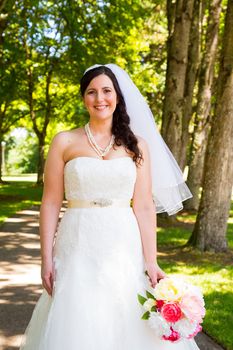 A bride poses for some portraits while wearing her wedding dress at a park outdoors just before here wedding ceremony.