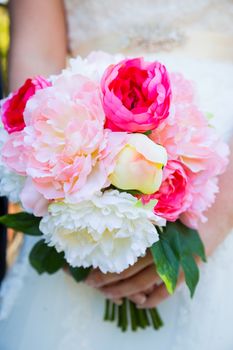 This bride holds her bouquet of white and pink flowers against her white wedding dress.