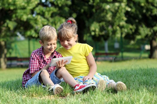 boy and little girl play with tablet pc in park