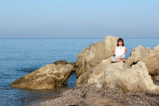 little girl sitting on a rock by the sea and meditate