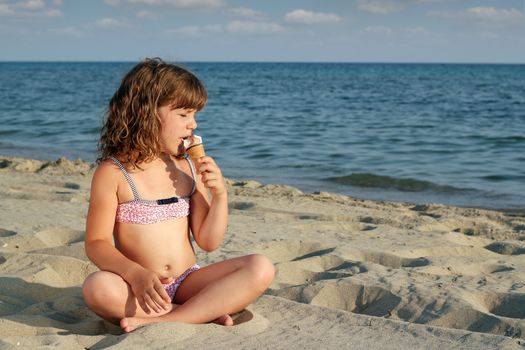 little girl sitting on beach and eat ice cream