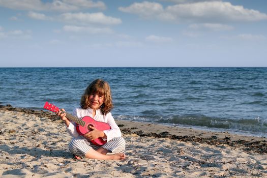 little girl sitting on beach and play guitar