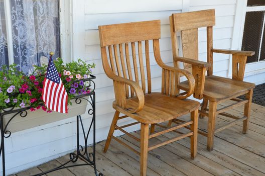 Two wooden chairs on old front porch with flowers and american flag