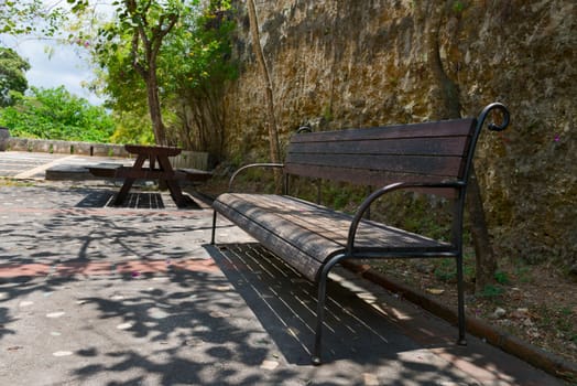 Bench in the sunny green park with wooden table on background