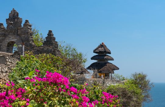 Pura Luhur Uluwatu Temple, Bali on cliffs above blue tropical sea with pink flowers on front 