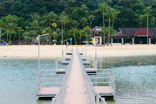 Wooden peer to modern clean tropical beach with palms on background. Selective focus on front.