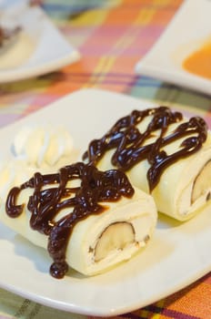 top view crepe rolls filled  with white cream and banana,   topping with chocolate  syrup served with whipping cream on dish