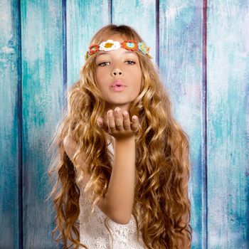 Blond hippie children girl blowing mouth with hand on blue grunge wood
