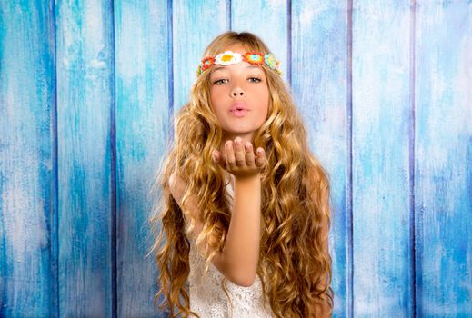 Blond hippie children girl blowing mouth with hand on blue grunge wood