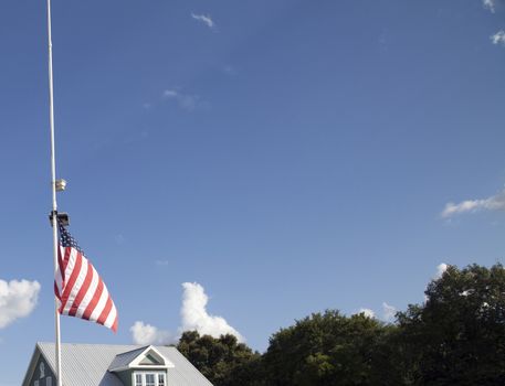 American flag at half mast with top of house and tree tops in the background