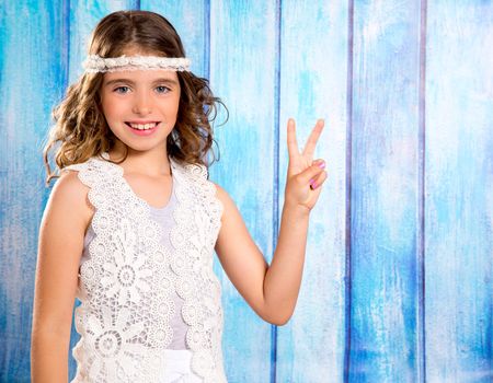 Brunette happy hippie children girl smiling with peace hand sign on blue wood