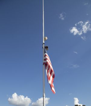 American flag at half mast with top of house and tree tops in the background