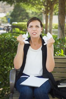 Frustrated and Upset Young Woman with Pencil and Crumpled Paper in Her Hands Sitting on Bench Outside.
