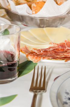 Closeup of typical spanish tapa, with slices of serrano ham and manchego cheese served in a plate, accompanied with a glass of Rioja red wine