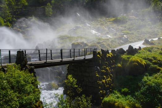 An old bridge covered in mist from a waterfall