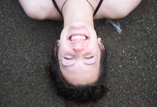 Closeup portrait of smiling young girl lying on sand near sea