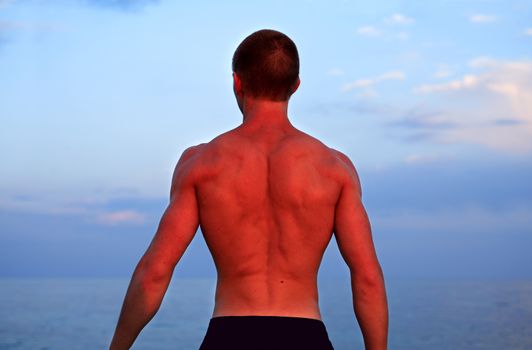 Nice back of young strong teenage athlete standing against sea