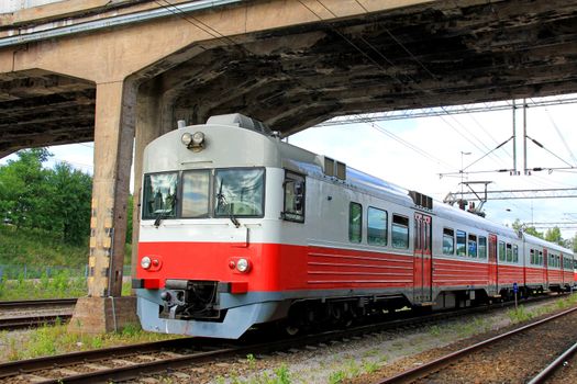 Red commuter train under bridge at railway station.