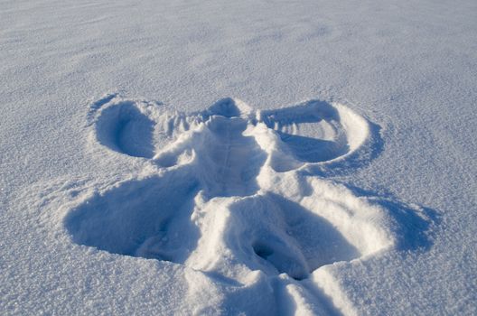 Angel silhouette on snow made by human. People make art in winter.
