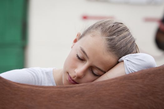 A girl resting her head on the back of her horse with eyes closed