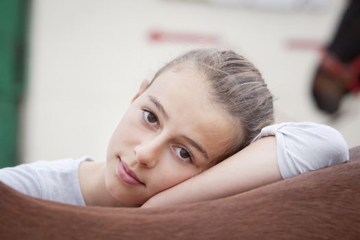 a teenage girl resting on the back of her horse, looking at camera