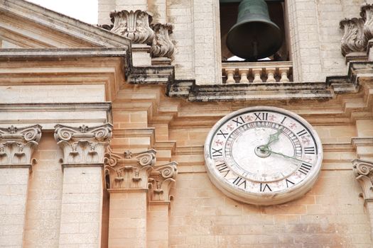 Close up of a church clock and church bell on a Maltese church