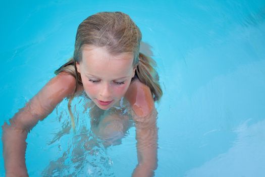 A young girl in a blue swimming pool. Space for text