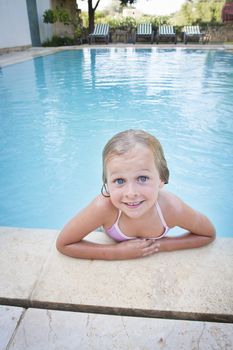 A smiling little girl at the edge of the swimmingpool, looking at the camera with big blue eyes