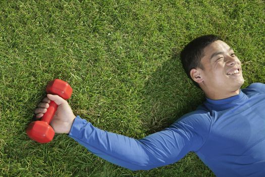 Young Athletic Man Lying Down in Grass with Dumbbells, Close Up
