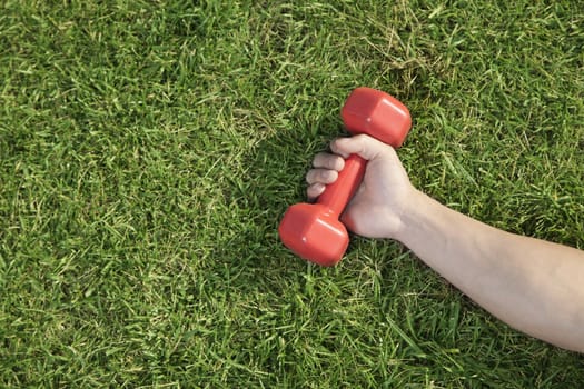 Close Up on Hand Holding Red Dumbbell in Grass