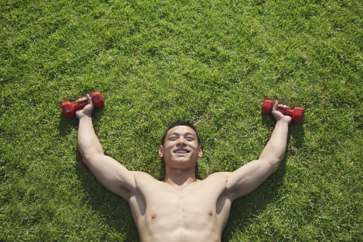 Shirtless Man Lying in Grass with Dumbbells in Beijing