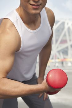 Young man exercising with dumbbell, close-up, midsection 