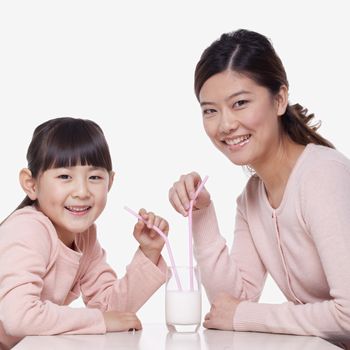 Portrait of mother and daughter sharing a glass of milk, studio shot