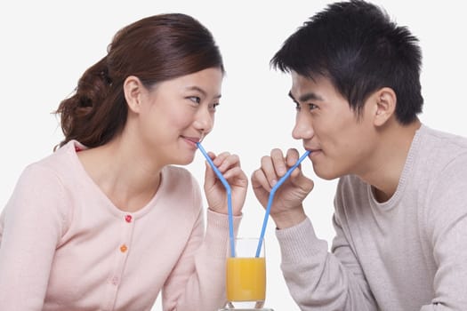 Young couple sharing a glass of orange juice, studio shot