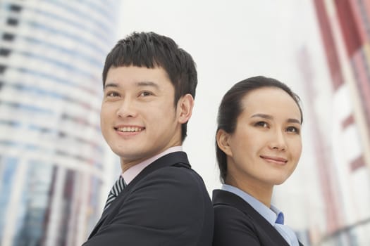 Young business man and woman standing back to back