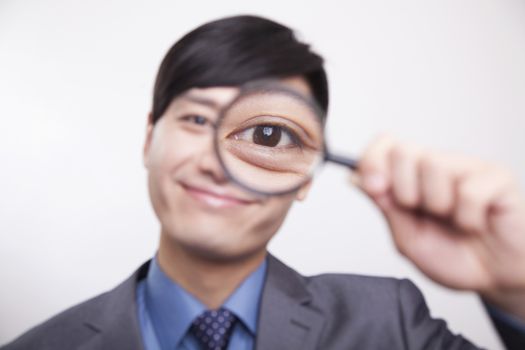 Young businessman looking through magnifying glass, studio shot