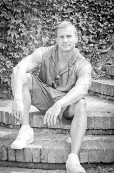 Handsome athletic young man smiling, sitting outdoors, black and white photo