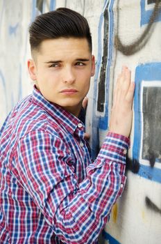 Handsome young man leaning next to colorful graffiti covered wall