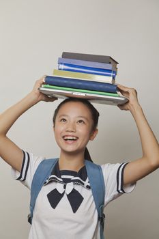 Girl smiling and holding bunch of notebooks and laptop on her head, Studio
