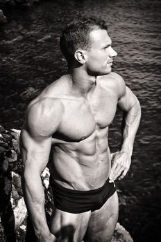 Attractive muscular young man by the sea, shirtless with bathing suit, black and white photo