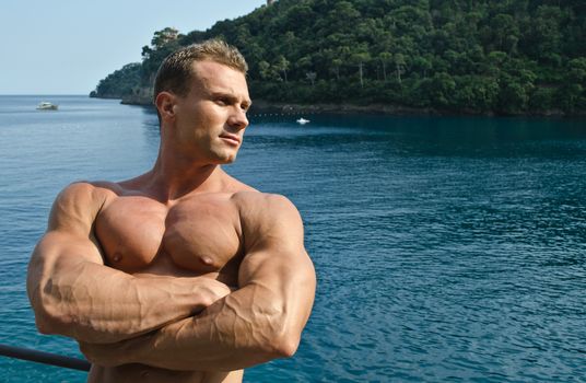 Attractive muscular young man with arms crossed and sea or ocean behind, large copyspace